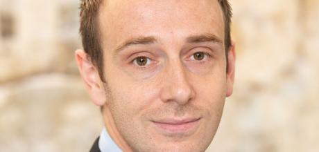 Man in a dark suit and blue tie, with a gentle smile.