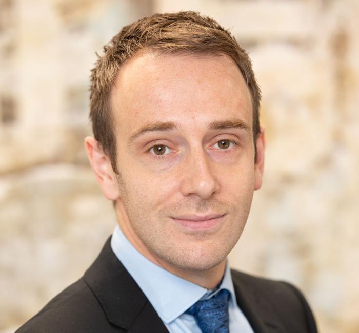 Man in a dark suit and blue tie, with a gentle smile.
