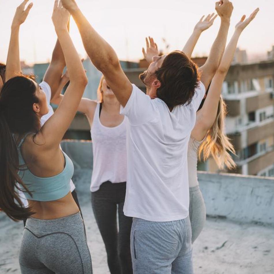 Friends celebrating on a city rooftop with arms raised at sunset.