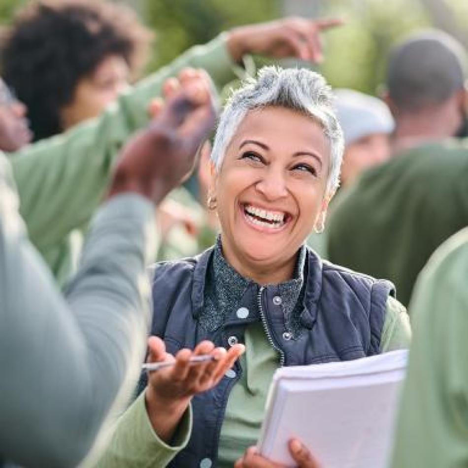 Photograph: Smiling woman with grey hair conversing animatedly with a group outdoors.