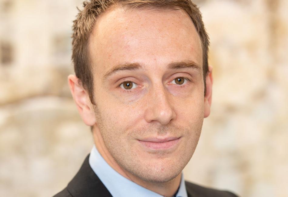 Man in a dark suit and blue tie, with a gentle smile.
