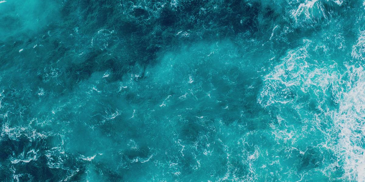 Photograph: Aerial view of deep blue-green and turquoise ocean with white foam.